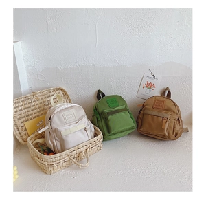 Three mini nylon backpacks for kids in beige green and caramel colors with letter patches