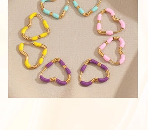 Detail view of colorful enamel heart earrings in gold finish on beige fabric