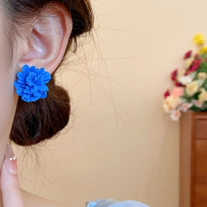 Gros plan d'une boucle d'oreille fleur en résine bleue portée par un mannequin en intérieur
