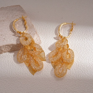 Close-up of golden leaf-shaped hoop earrings with zircon crystals on a natural stone base