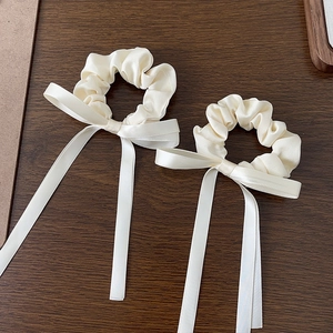 Detail of cream white satin scrunchies with long silk ribbons on wooden background