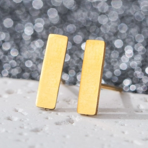 Macro shot of minimalist gold rectangular bar earrings on textured white stone surface