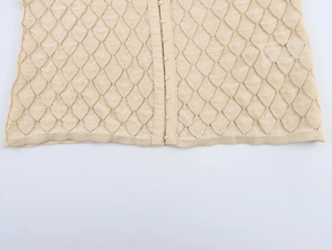 Detail of beige hollow knit fabric featuring diamond texture and metal hook-and-eye closures