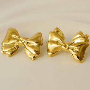 Macro detail of high-shine 18k gold plated stainless steel bow earrings on beige background