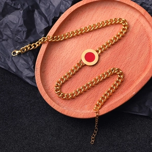 Detail of a gold Cuban link chain with a red round pendant on a wooden tray