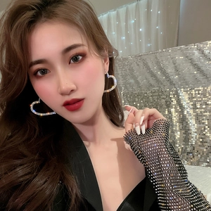 Close-up of sparkling oversized heart-shaped rhinestone earrings worn by a party model