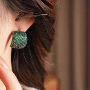 Gros plan de boucles d'oreilles serties de cristaux vert émeraude portées par un mannequin