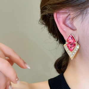 Close-up of pink diamond-shaped stud earrings with gold plating on female ear