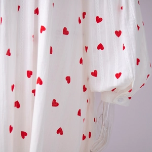 Détail de la manche lanterne avec imprimé cœur rouge et bouton sur la robe blanche
