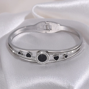 Macro detail of silver titanium steel open bangle with black heart and crystal accents