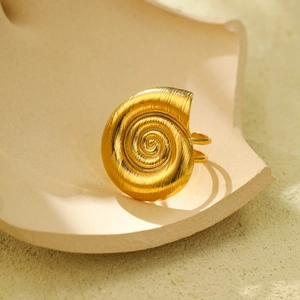 Macro shot of gold spiral nautilus ring with textured ridges on a beige stone base