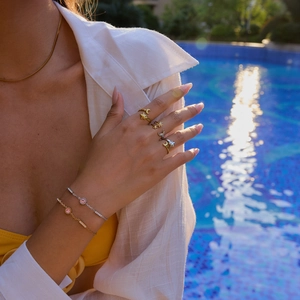 Close-up of gold star and moon rings with pink zircon bracelet by a blue pool