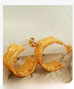Close-up of gold 18K textured C-shaped hoop earrings with wavy hammered surface