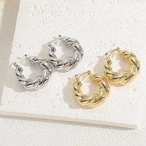 Minimalist twisted hoop earrings in gold and silver finish on a textured stone base