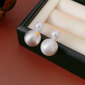 Macro detail of silver pearl earrings featuring matte texture and dual-size beads design