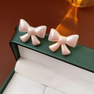 Macro shot of pink pearlescent bow earrings resting on a luxury dark green jewelry box