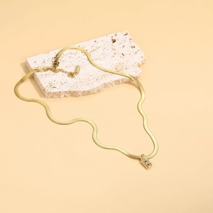 Detail of gold letter B pendant with zircon on a snake chain over beige stone