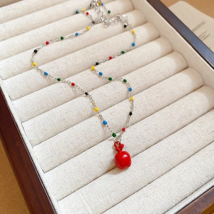 Vue détaillée d'un collier argenté avec pendentif pomme rouge et perles colorées en boîte
