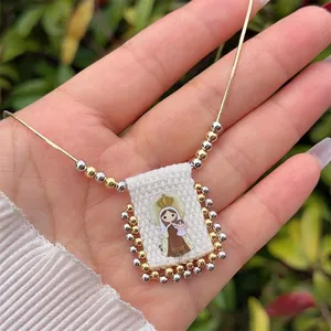Macro shot of an 18K gold-plated scapular necklace featuring a religious Our Lady of Mount Carmel icon