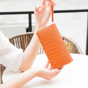 Detailed view of an orange crocodile embossed long wallet with a wrist strap and zipper