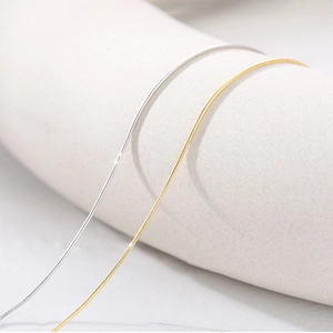 Detailed view of fine s925 silver and gold snake bone chains on a ceramic holder