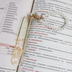 Detailed view of clear resin bookmark with gold flakes and dried flowers on a book page