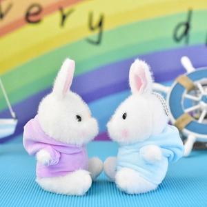 Close-up of two adorable white plush bunny keychains wearing purple and blue hoodies