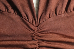 Detail shot of deep V-neck and ruched texture on dark brown sleeveless knit dress
