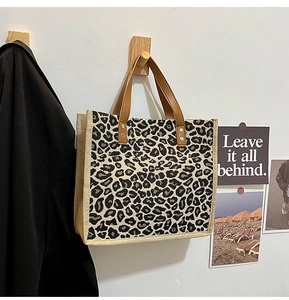 Detailed texture of leopard print linen tote bag with brown leather handles hanging on wall