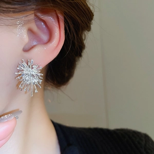 Close-up of sparkling silver firework earrings with inlaid crystals worn by a woman