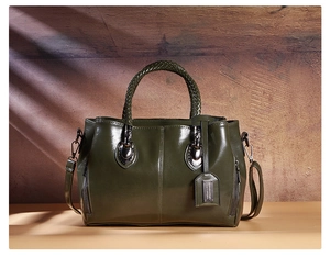 Detail of a dark green leather Boston bag with woven handle and side zippers