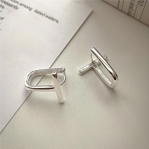 Close-up of minimalist silver T-shaped geometric hoop earrings on textured beige leather