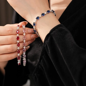 Detail of elegant silver-tone bracelets with blue, red, and pink zircon gemstones on a wrist
