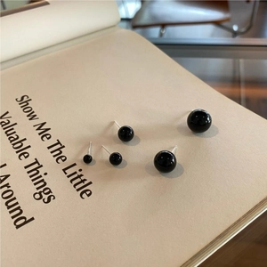 Detailed view of three sizes of black onyx ball stud earrings on a vintage book page