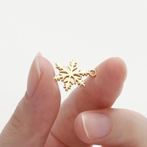 Close-up of a small 18K gold-plated snowflake pendant held to show scale for DIY jewelry