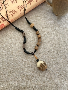 Detail shot of Zen-style pine nut wooden bead necklace with a lotus pendant over calligraphy