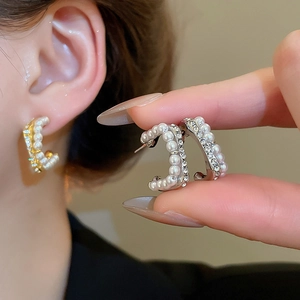 Close-up of C-shaped pearl earrings with crystal pavé on gold and silver metal base