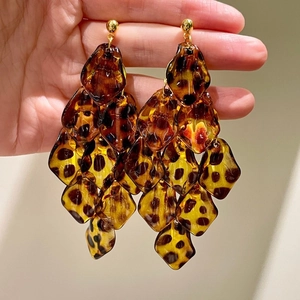 Detail of amber leopard print acrylic layered diamond earrings with golden studs