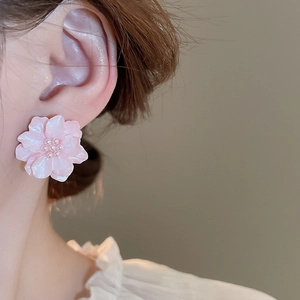 Close-up of pink layered flower stud earrings with a pearl center on a model's ear