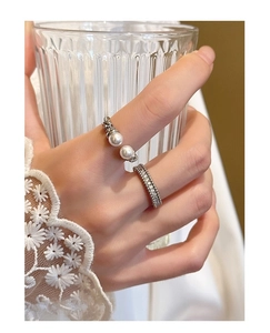 Detail of silver pearl and zircon stackable rings worn on a hand holding a glass cup