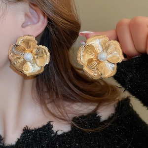 Oversized gold flower earrings with large pearl center and radiant metal texture