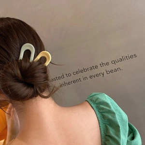 Detail of matte candy-colored U-shaped hairpins in light green and yellow on a bun hairstyle