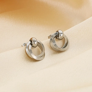 Detailed close-up of silver geometric interlaced hoop earrings on beige satin fabric