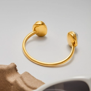 Détail d'un bracelet ouvert doré avec incrustation de perle baroque sur fond blanc