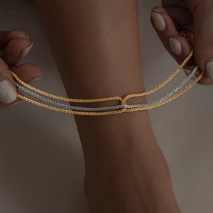 Detailed view of layered gold and silver mixed woven chain anklets on model ankle