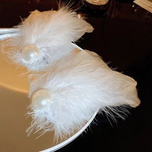 Macro shot of elegant white feather hair clips with pearls on a golden vintage tray