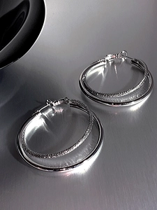 Detail of silver double-hoop earring showing smooth mirror and braided texture contrasts
