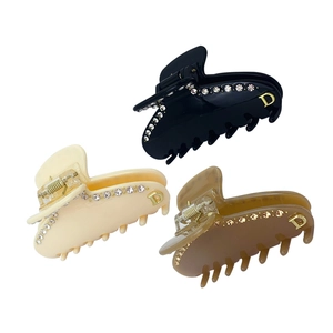 Dettaglio di tre mollette per capelli nere, beige e marroni con strass e decorazione in D