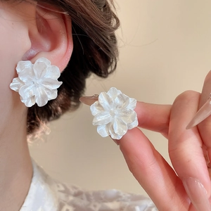 Dettaglio di orecchini a lobo a fiori bianchi con petali perlati indossati da una modella