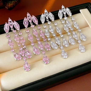 Detailed view of silver zircon drop tassel earrings in pink and white on beige velvet